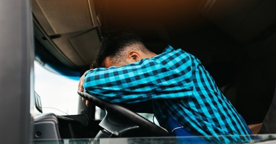 Man leaning over steering wheel with his head down.