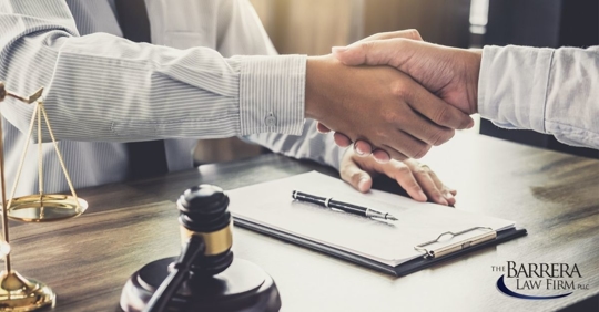 Two men shaking hands over a desk that has a clipboard and judges gavel on the desk.