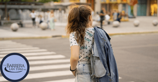 image of the back of a young teenage girl with long brown hair with denim jacket over her shoulder crossing a crosswalk