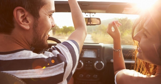 Young man and woman driving in a convertible car smiling at each other