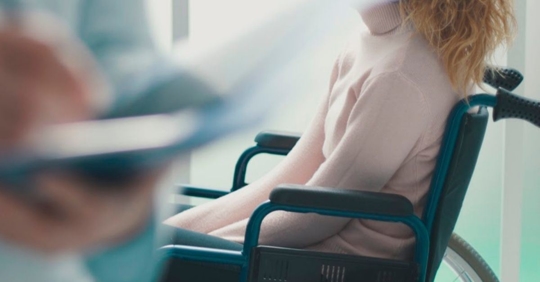 a doctor taking notes with a woman in the background in a wheelchair
